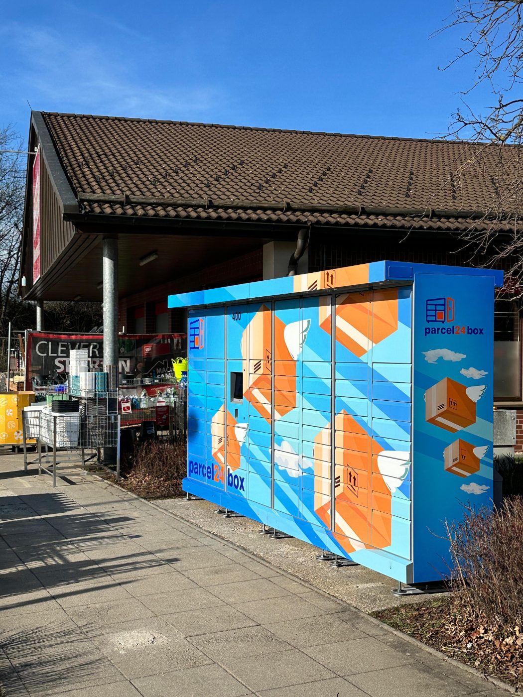 Digitale Paketstation von parcel24box vor einem Baumarkt, frequentierter Einzelhandelsstandort